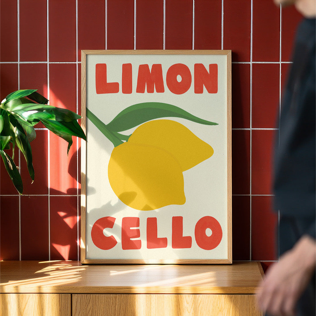 Framed artwork with a lemon and text on a wooden surface against a red tiled wall.