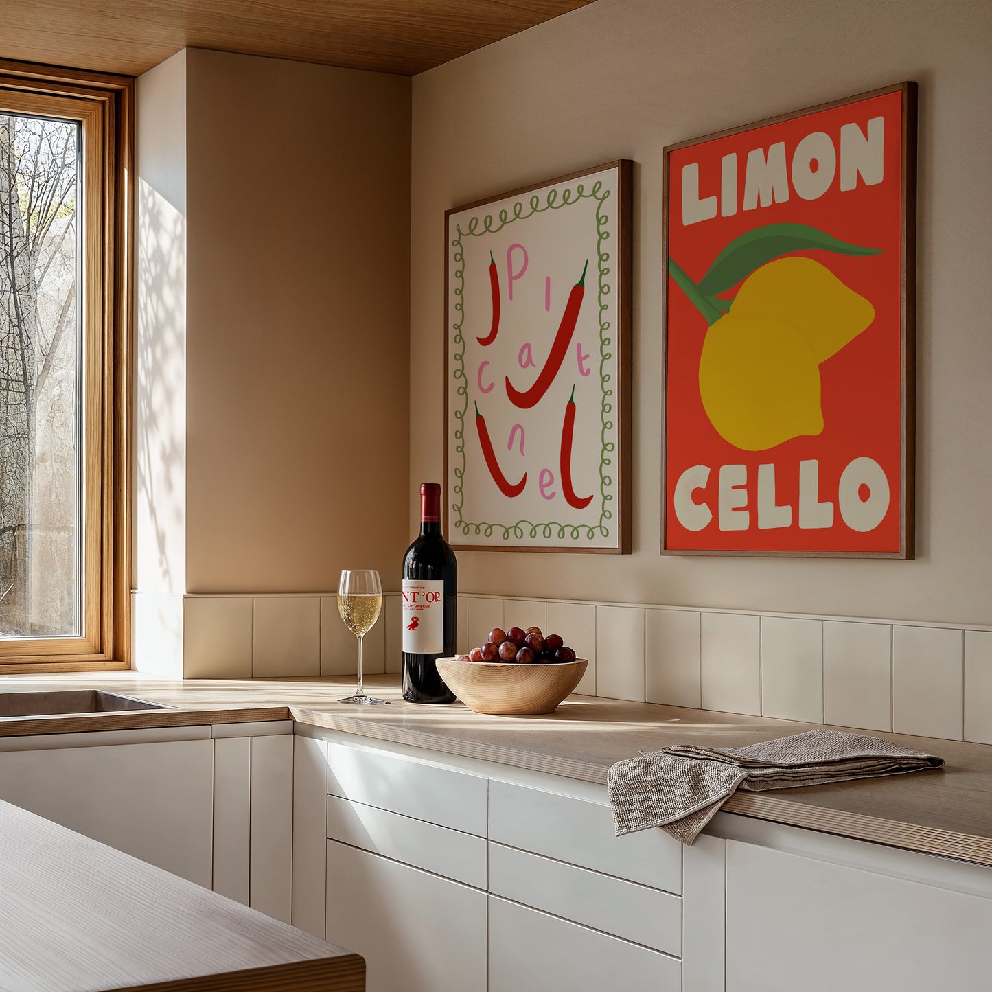 Modern kitchen with wine bottle, glass, and fruit on a countertop, featuring two colorful artworks on the wall.
