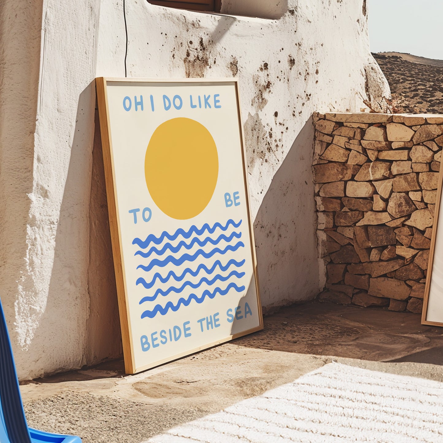 Framed artwork with a sun and wave design leaning against a stone wall.