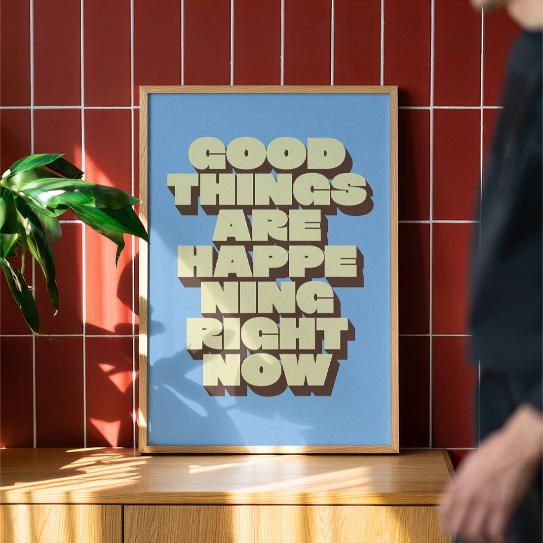 Framed poster with 'Good things are happening right now' text on a red tiled wall.