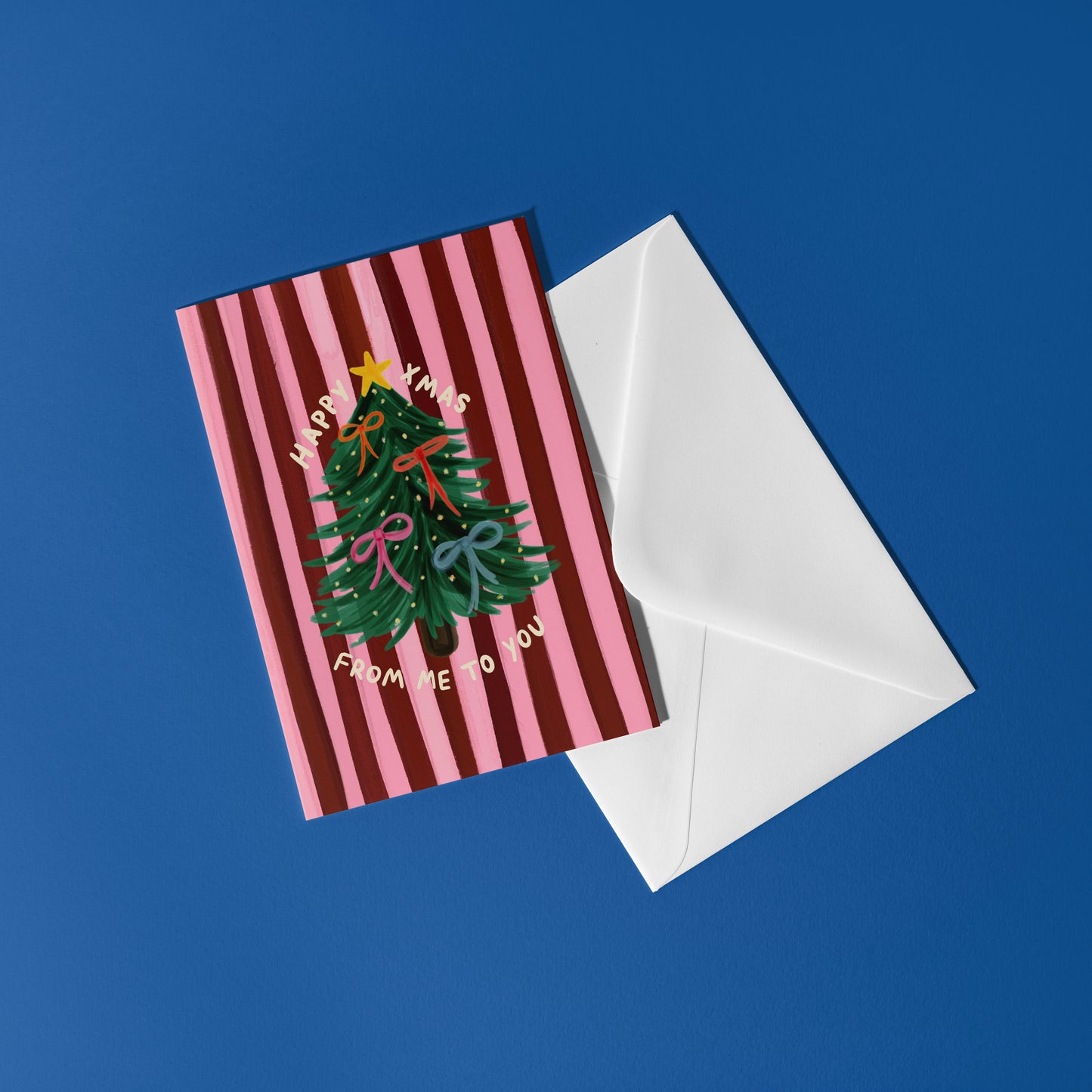 Greeting card with Christmas tree design and striped pattern, accompanied by a white envelope on a blue background.