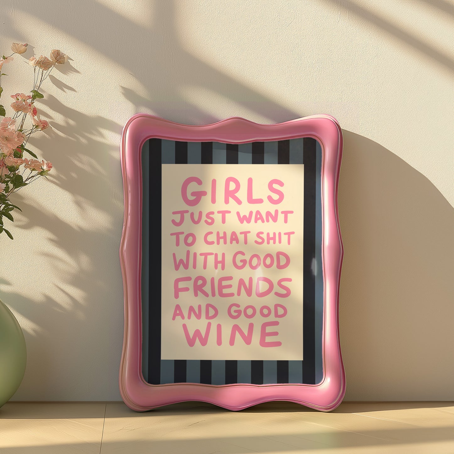 Framed quote on a wall with pink frame and text 'GIRLS JUST WANT TO CHAT SHIT WITH GOOD FRIENDS AND GOOD WINE'.