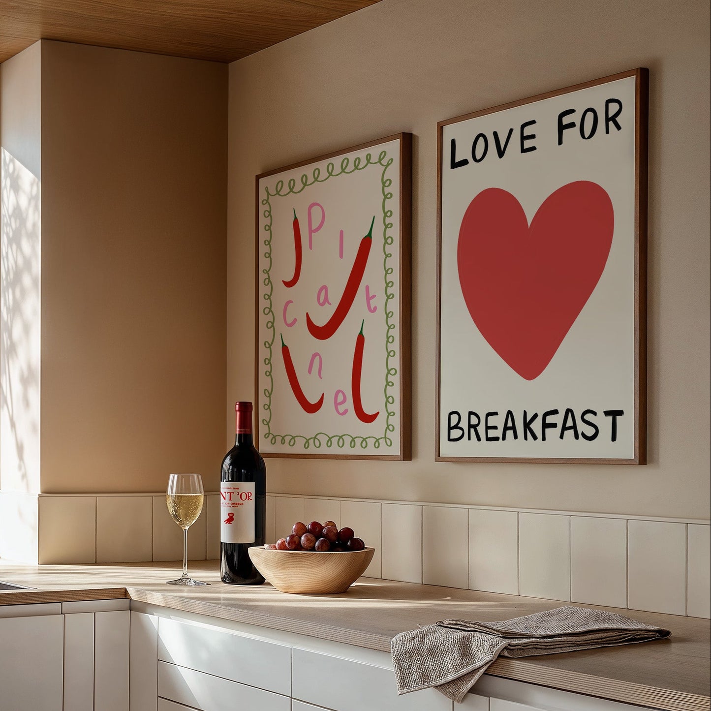 Modern kitchen with wine bottle, grapes, and two framed artworks on the wall.
