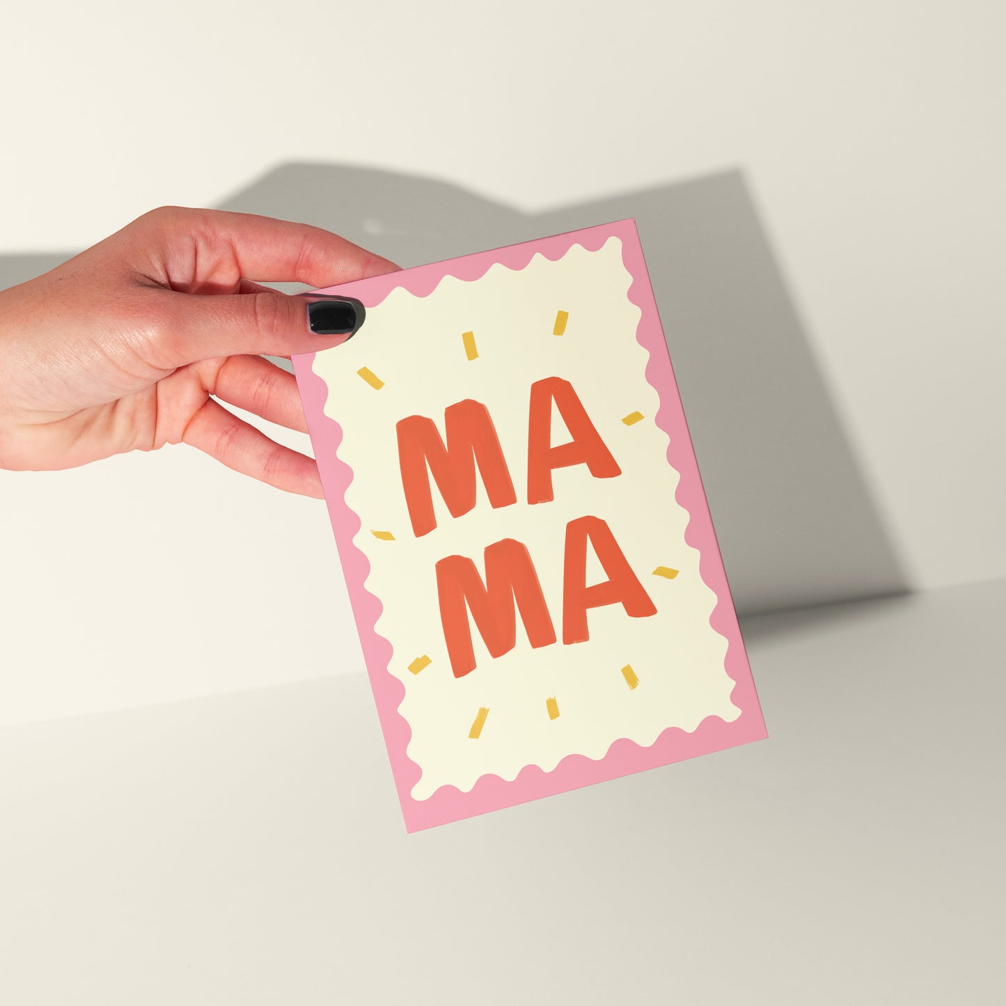 Hand holding a card with 'MAMA' text on a plain background