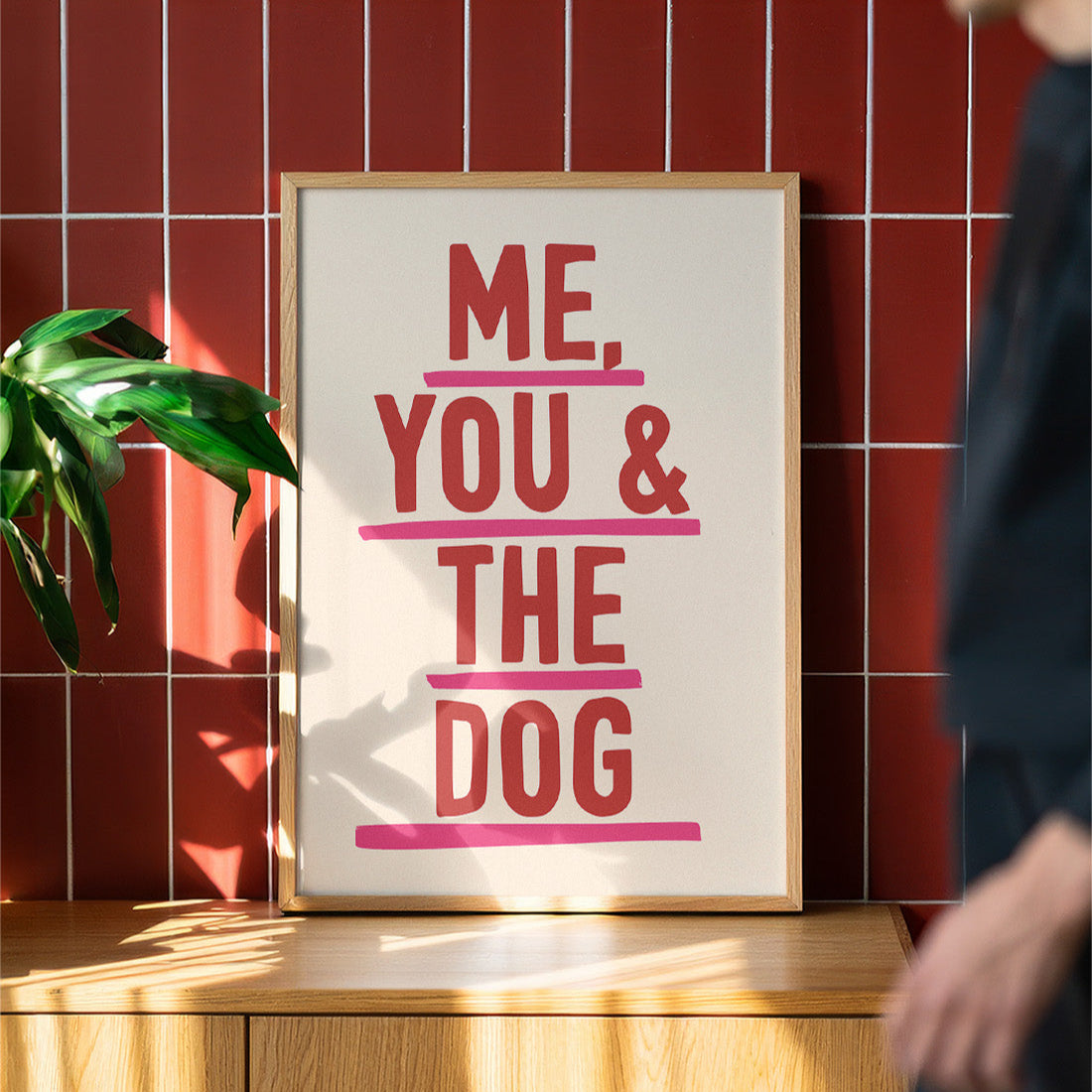 Framed poster with 'Me, You & The Dog' text on a wooden surface with a red tiled wall background.