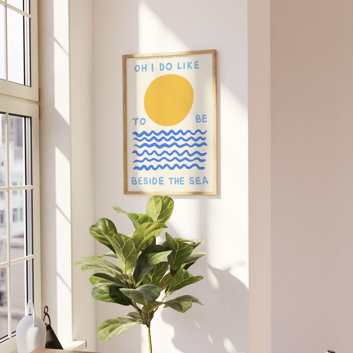 Framed artwork with a sun and wave design on a wall next to a plant and window.