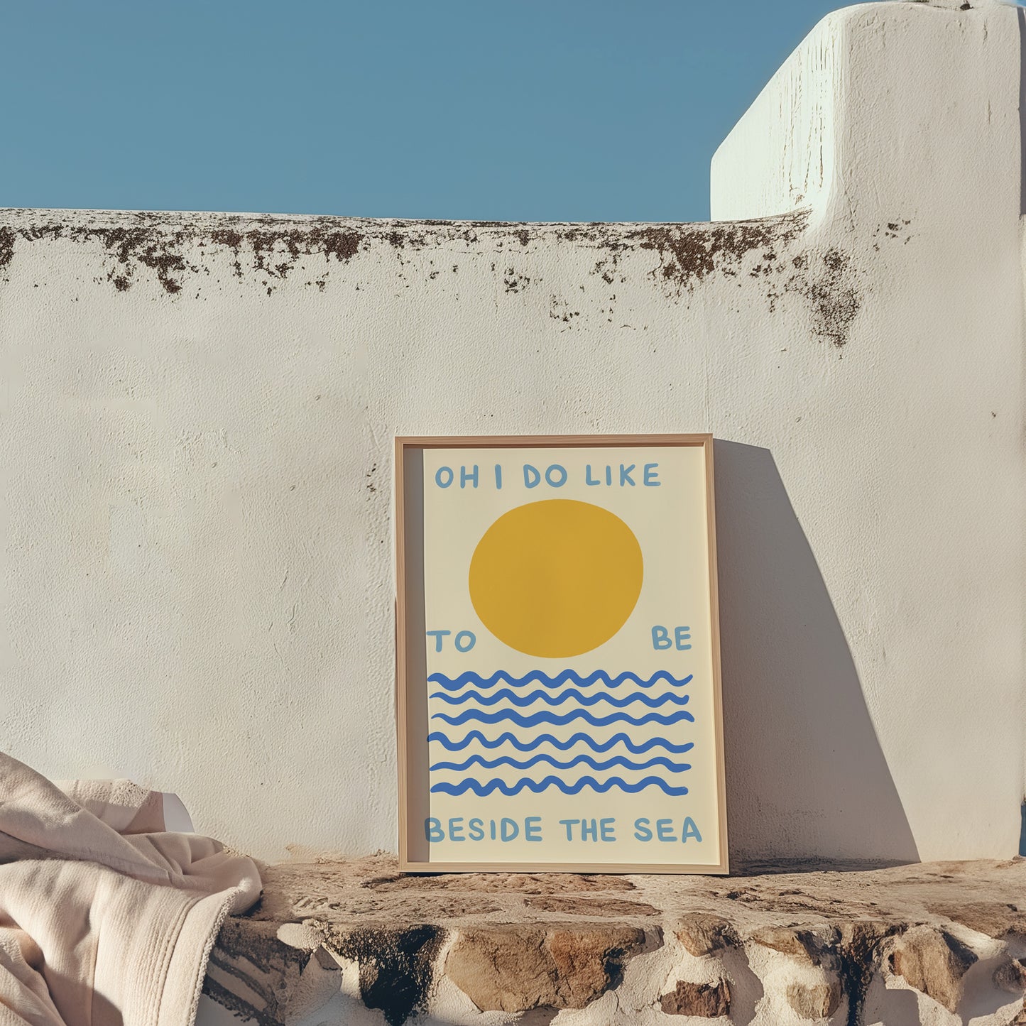 Framed artwork with a sun and wave design on a stone ledge against a white wall.