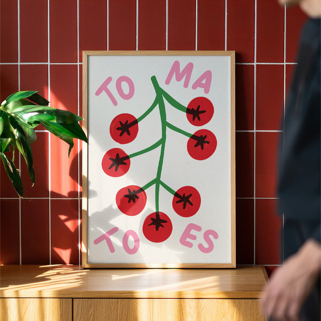 Framed artwork with red berries and pink text on a wooden surface against a red tiled wall.