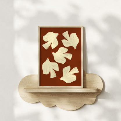 Framed artwork with white abstract shapes on a brown background, displayed on a wooden shelf.