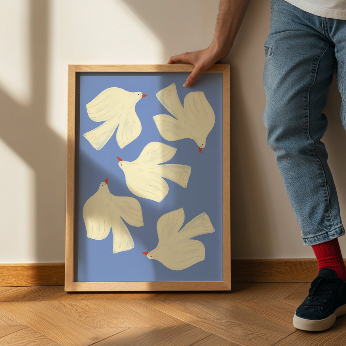 Framed artwork of white birds on a blue background, held by a person.