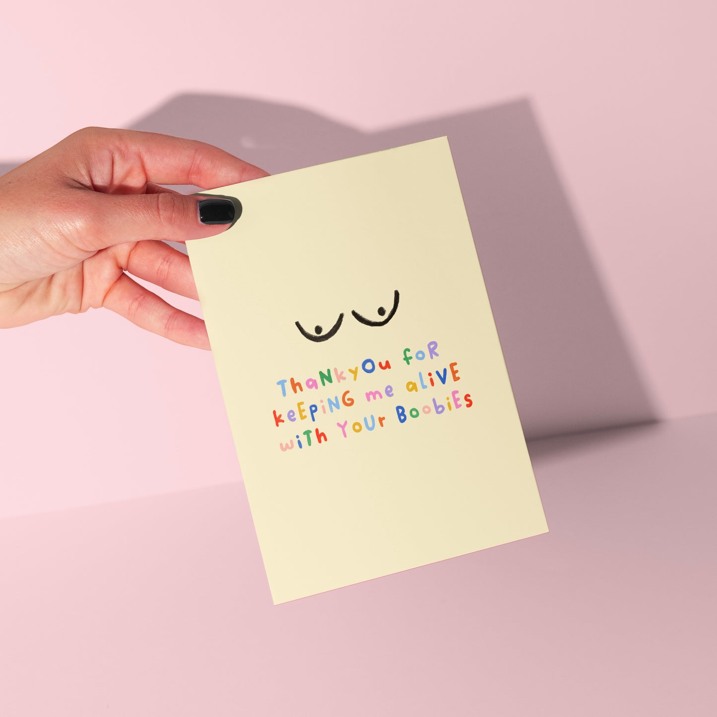 Hand holding a light yellow card with text and a smiley face on a pink background