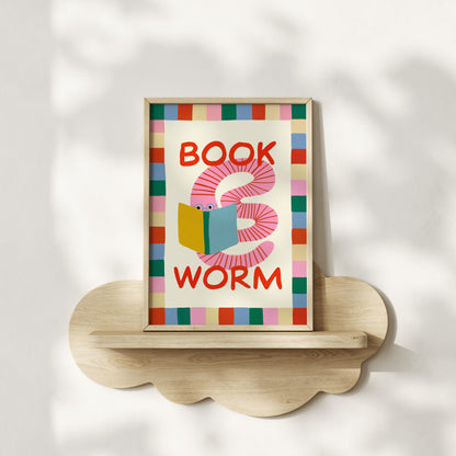 Framed artwork with a colorful design of a worm reading a book, labeled 'Book Worm', on a wooden shelf.