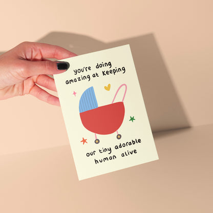 Hand holding a card with a baby buggy illustration and text on a beige background