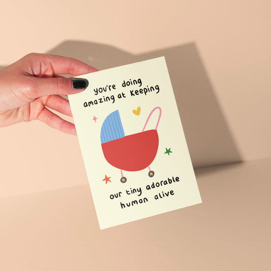 Hand holding a card with a baby buggy illustration and text on a beige background