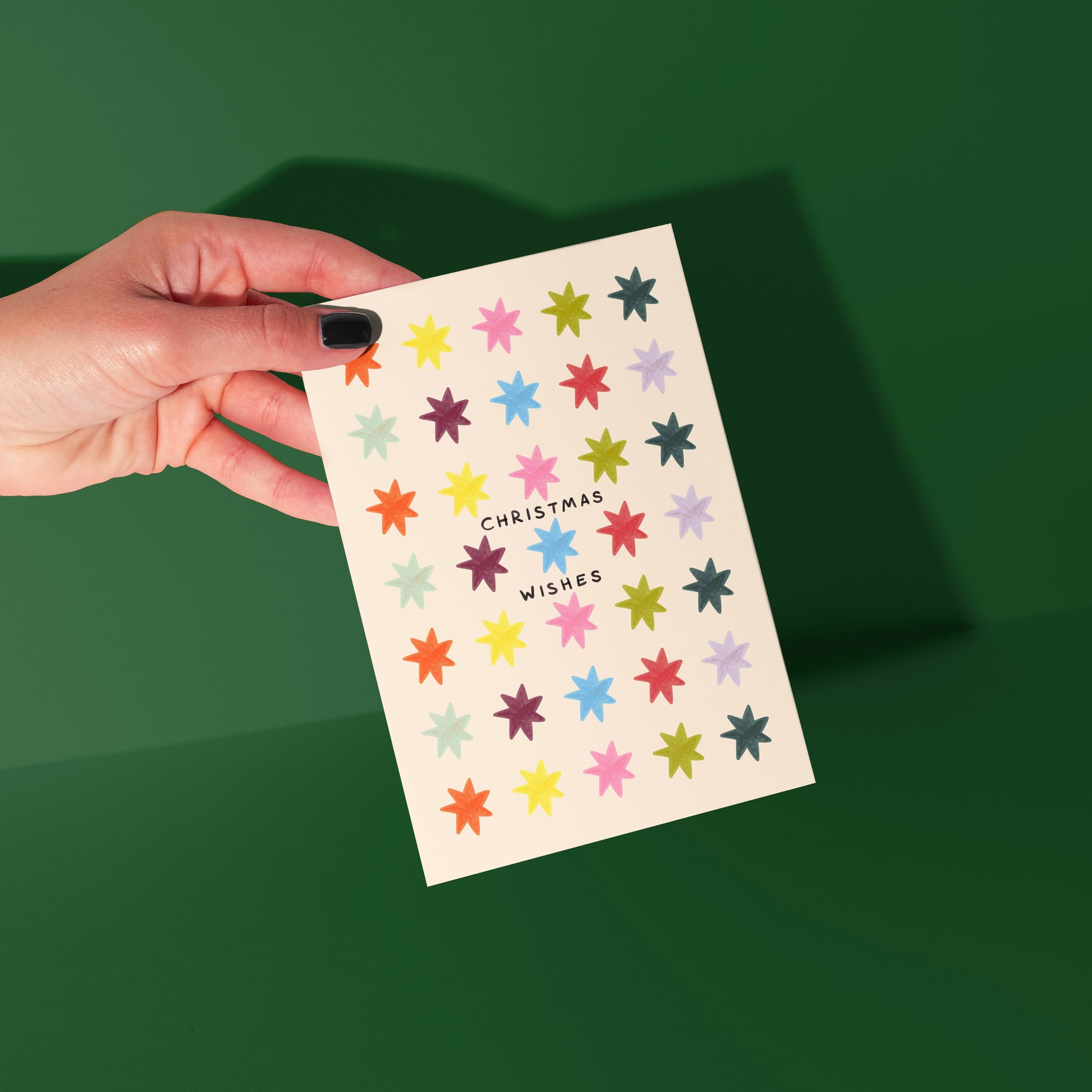 Hand holding a card with colorful star patterns and 'Christmas Wishes' text on a green background