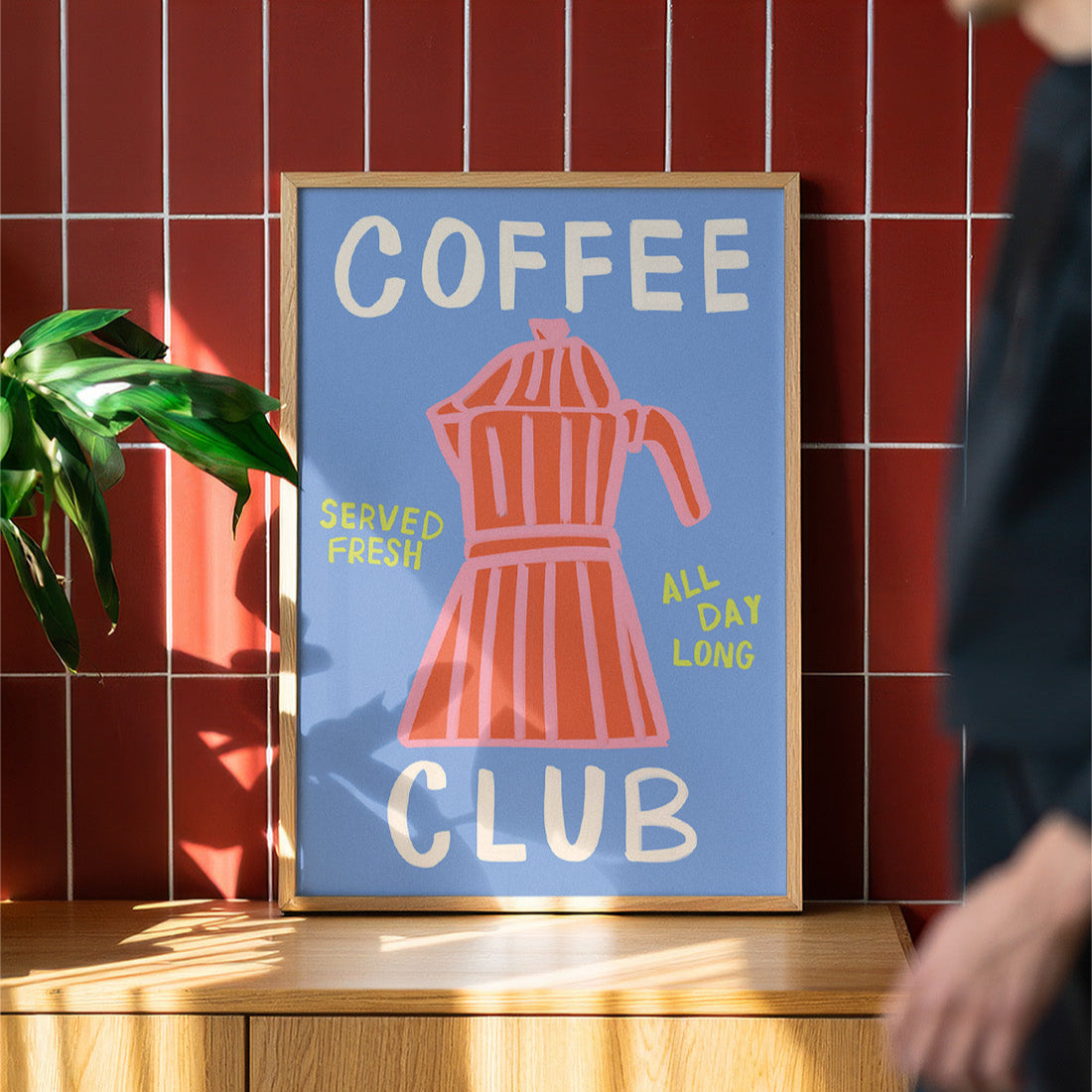 Framed poster with coffee-themed design on a wooden surface against a red tiled wall.