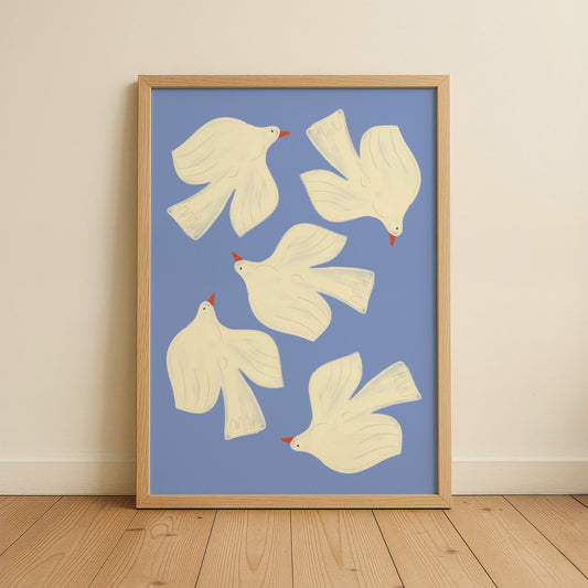 Framed artwork with white dove illustrations on a blue background, displayed on a wooden floor.