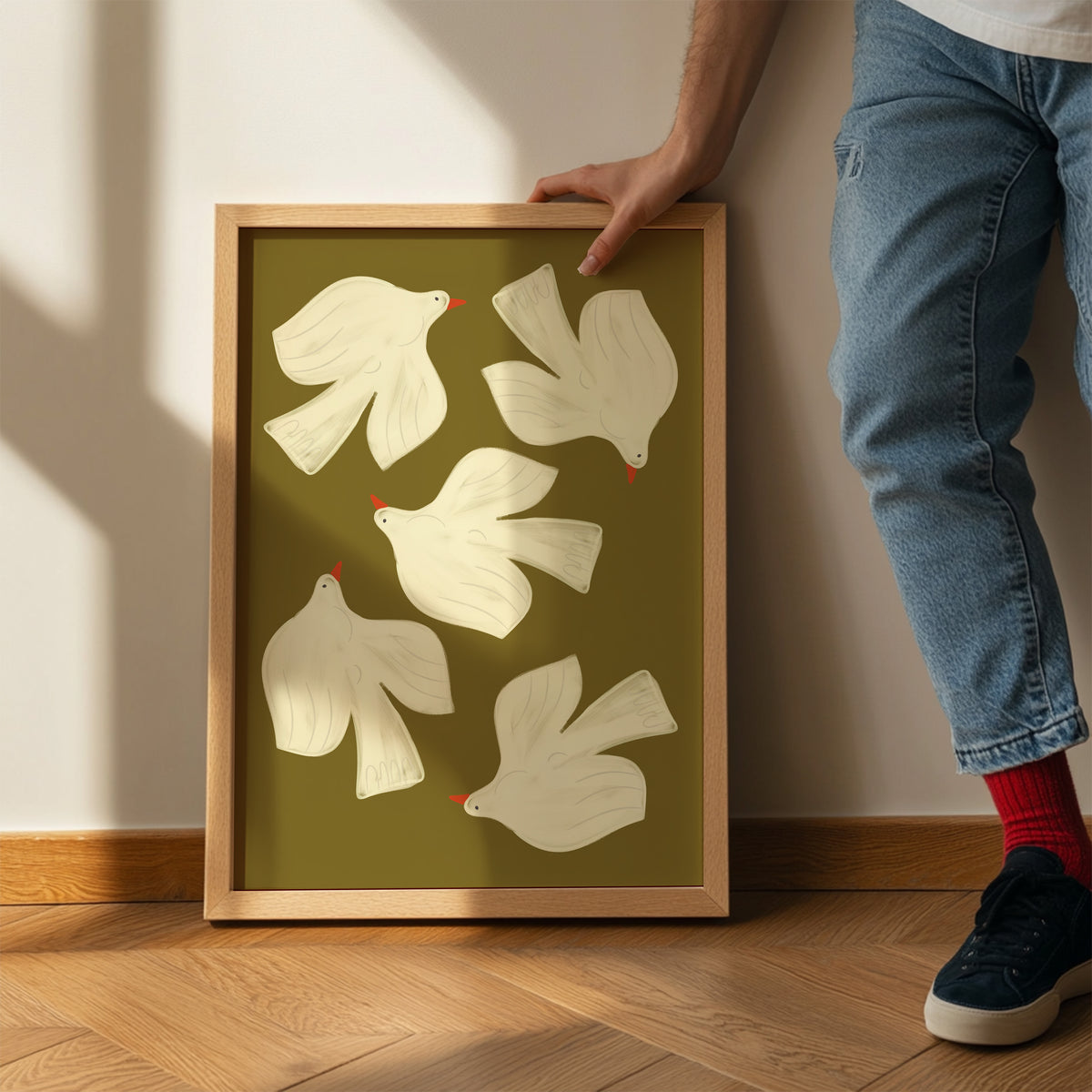 Framed artwork of white birds on a green background, held by a person.