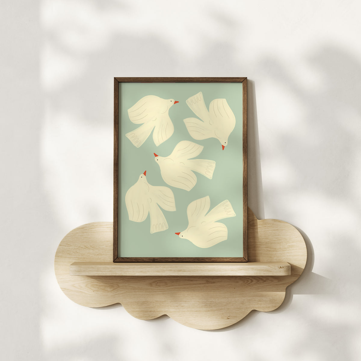 Framed artwork with white birds on a light green background, displayed on a wooden shelf.