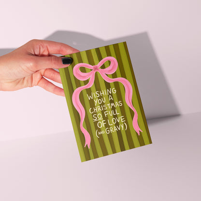 Hand holding a Christmas card with a pink bow and text on a white background