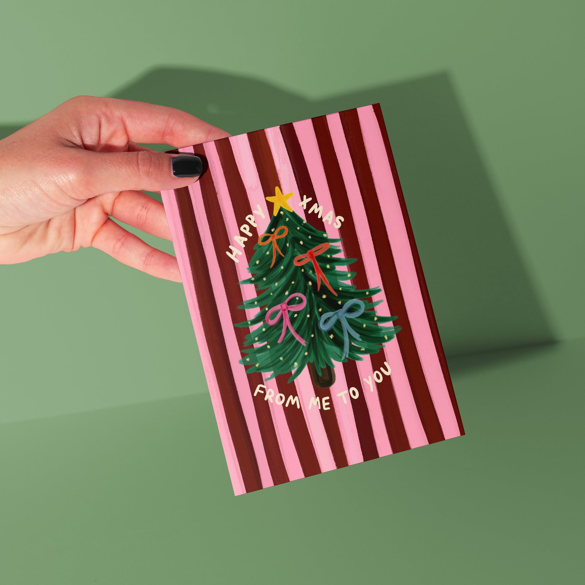 Hand holding a striped card with a Christmas tree design on a green background