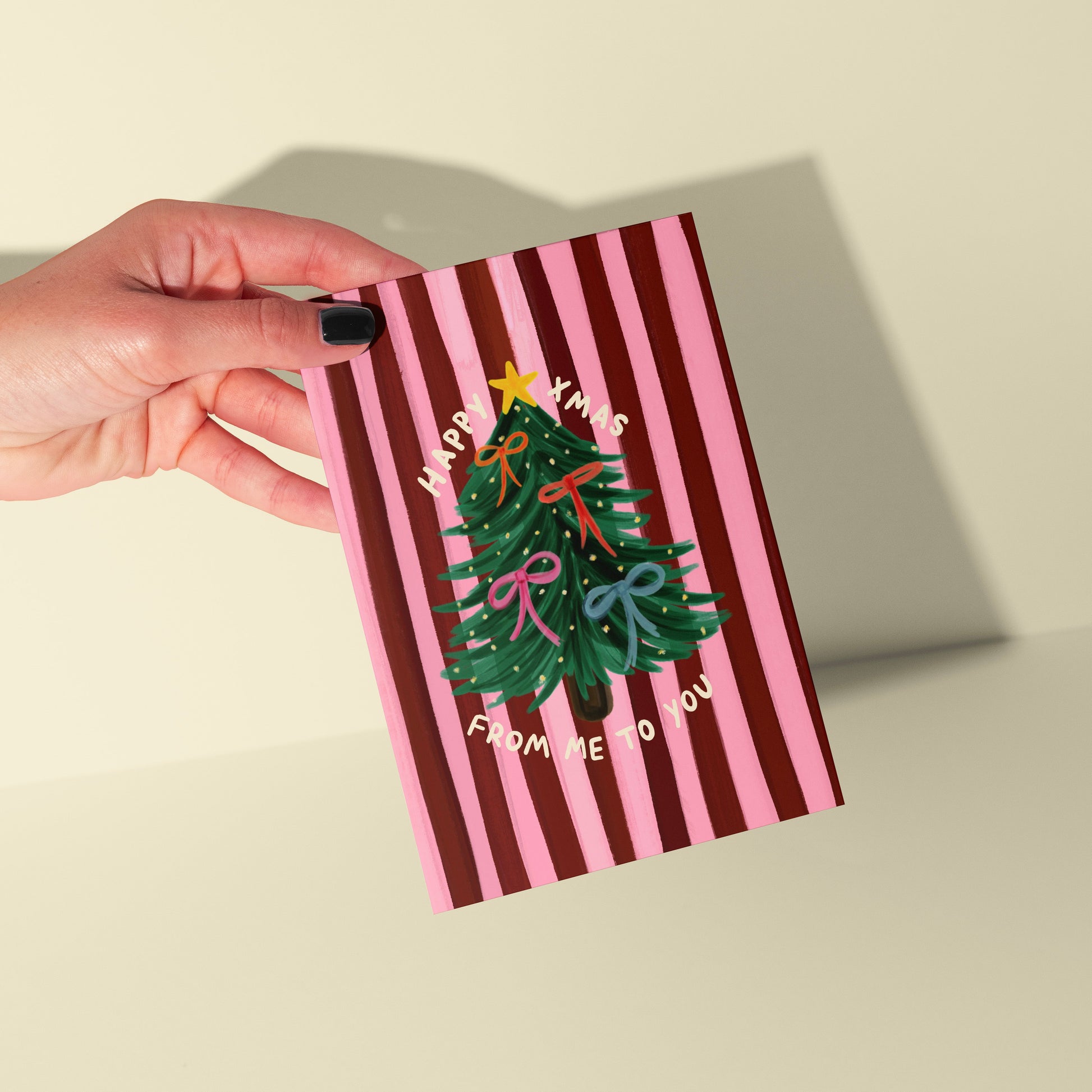 Hand holding a striped card with a Christmas tree design on a beige background