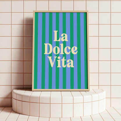 Framed artwork with 'La Dolce Vita' text on a striped background, placed on a tiled surface.