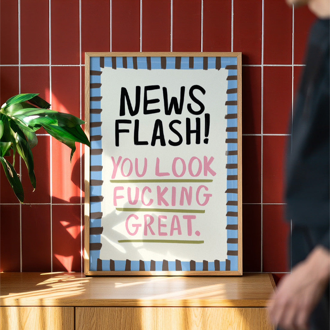 Framed poster with motivational text on a wooden surface against a red tiled wall.